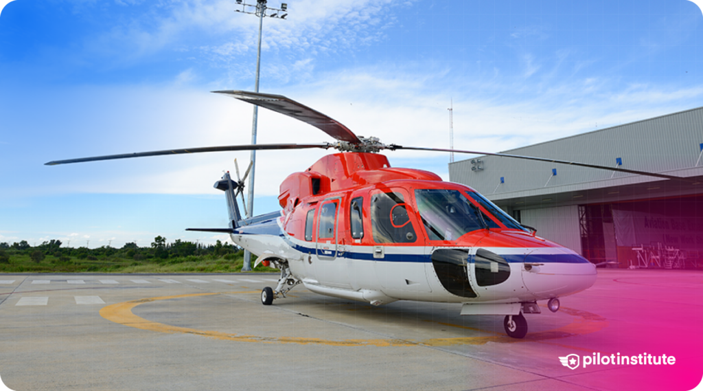 Red and white helicopter parked on a helipad in front of an airport hangar.